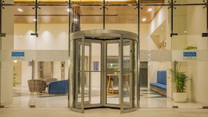 A revolving door with glass panels, a blue sofa, and a potted plant in a lobby area. - Keys Prima by Lemon Tree Hotels, Pimpri Pune (Pune)