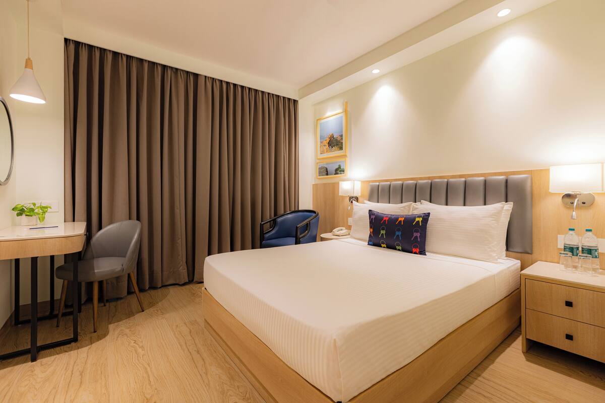 Habitación de hotel con una cama grande, un escritorio, una silla, una mesita de noche y una ventana con cortinas.