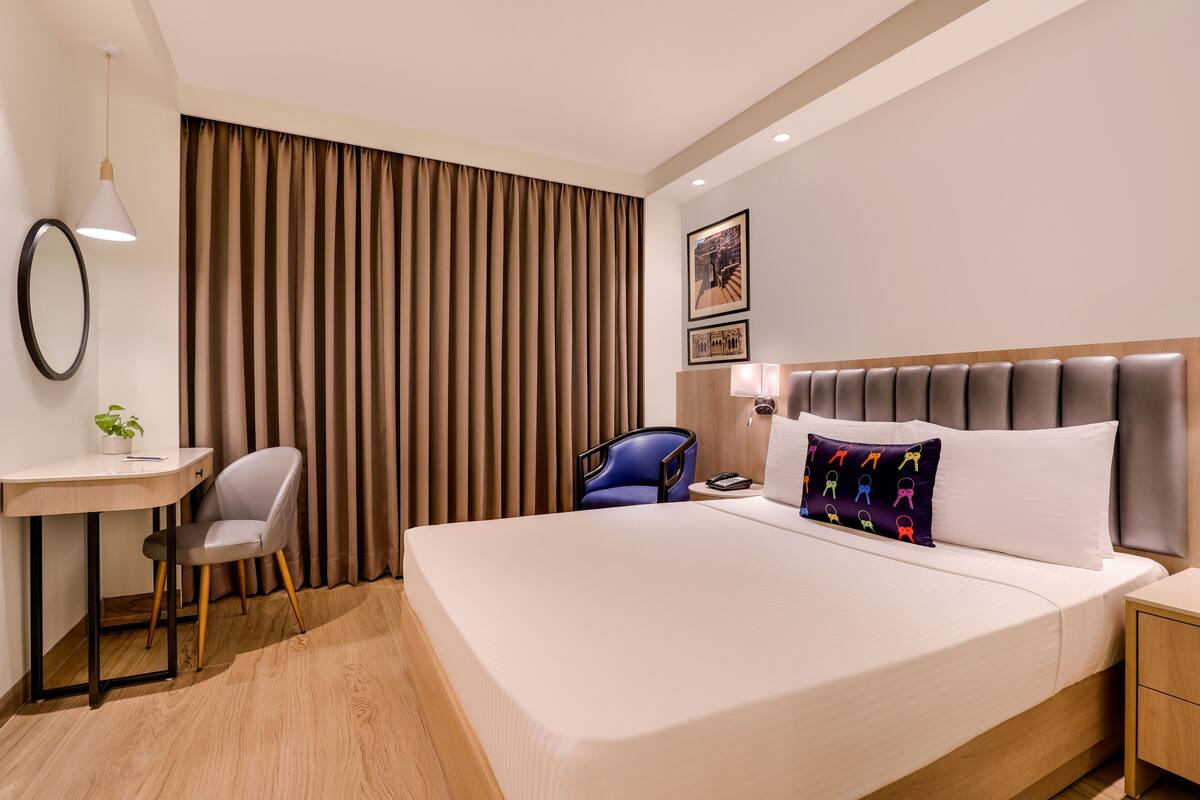 Habitación de hotel con una cama grande, un escritorio con silla, una lámpara y un espejo instalado en la pared.