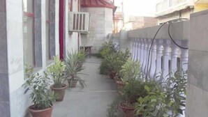 Un pasillo estrecho con plantas en macetas a ambos lados, suelo de hormigón y un toldo rojo.