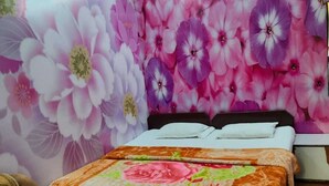 Un dormitorio con papel tapiz floral, una cama con cubrecama floral, suelo de madera y una mesita de noche.