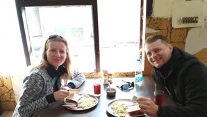 Dos personas sentadas a una mesa con platos de comida, una bebida y salsas.