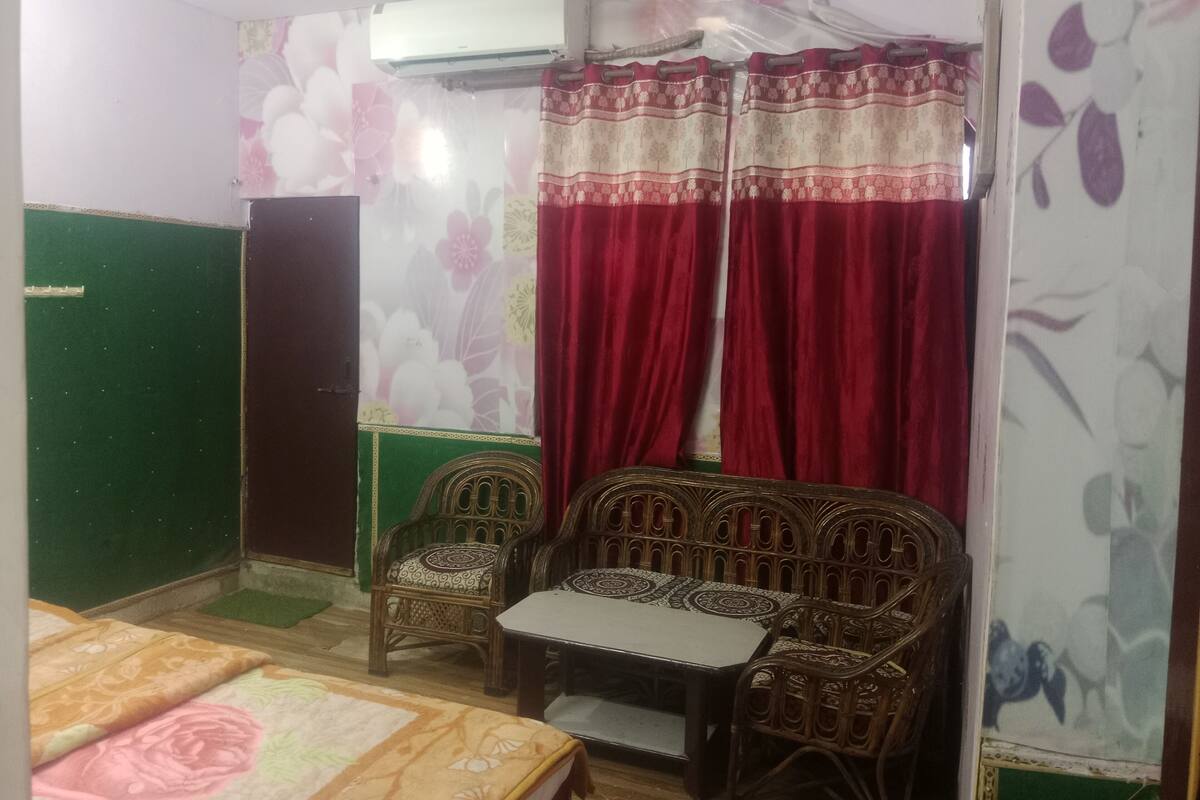 A room with a bed, two chairs, a table, a green door, and a floral wall.