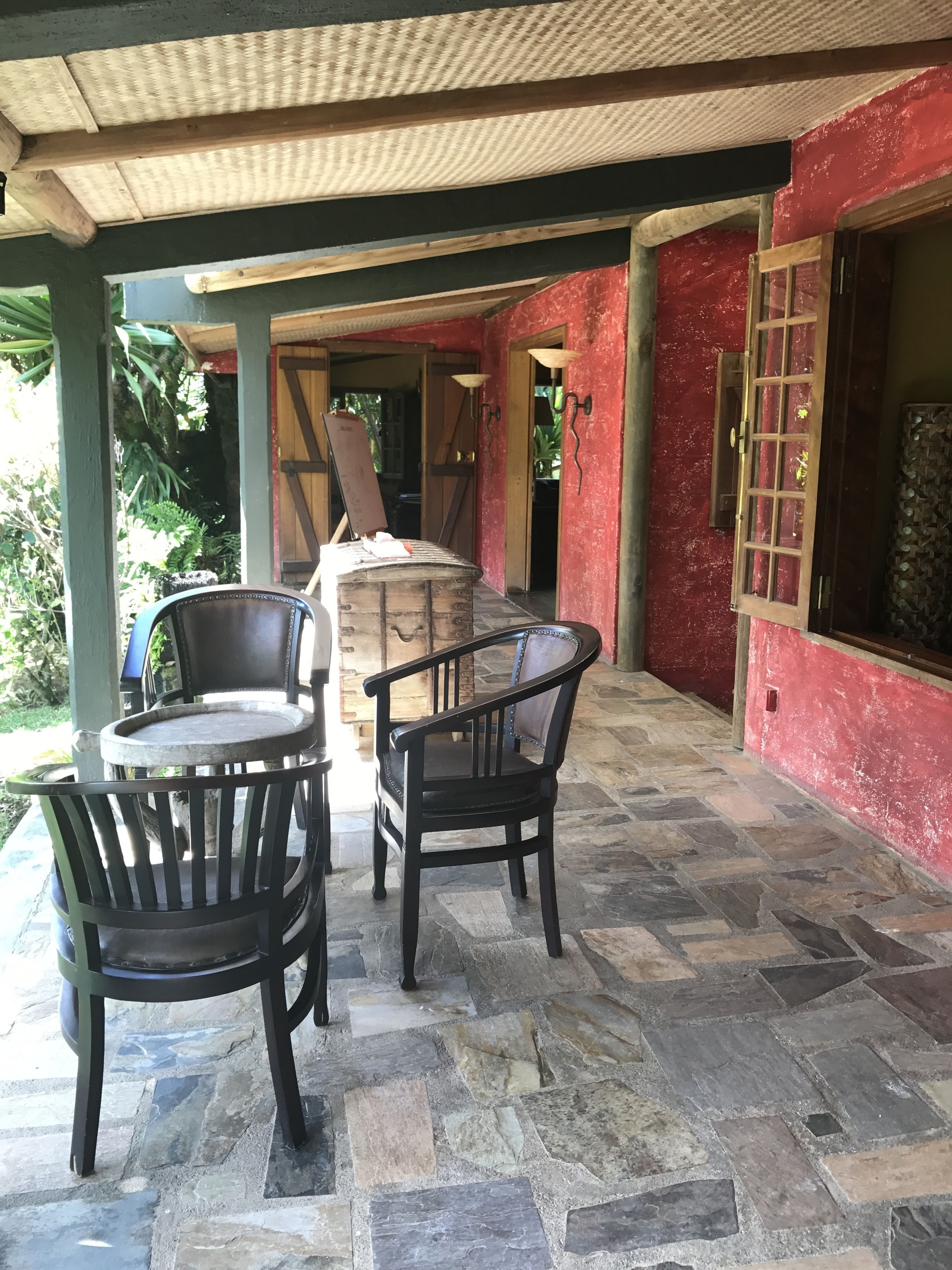 A covered patio area with stone flooring, two wooden chairs, and a table.