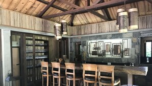 Angolo bar rustico con sedie di legno, bancone bar e parete in pietra con opere d'arte.