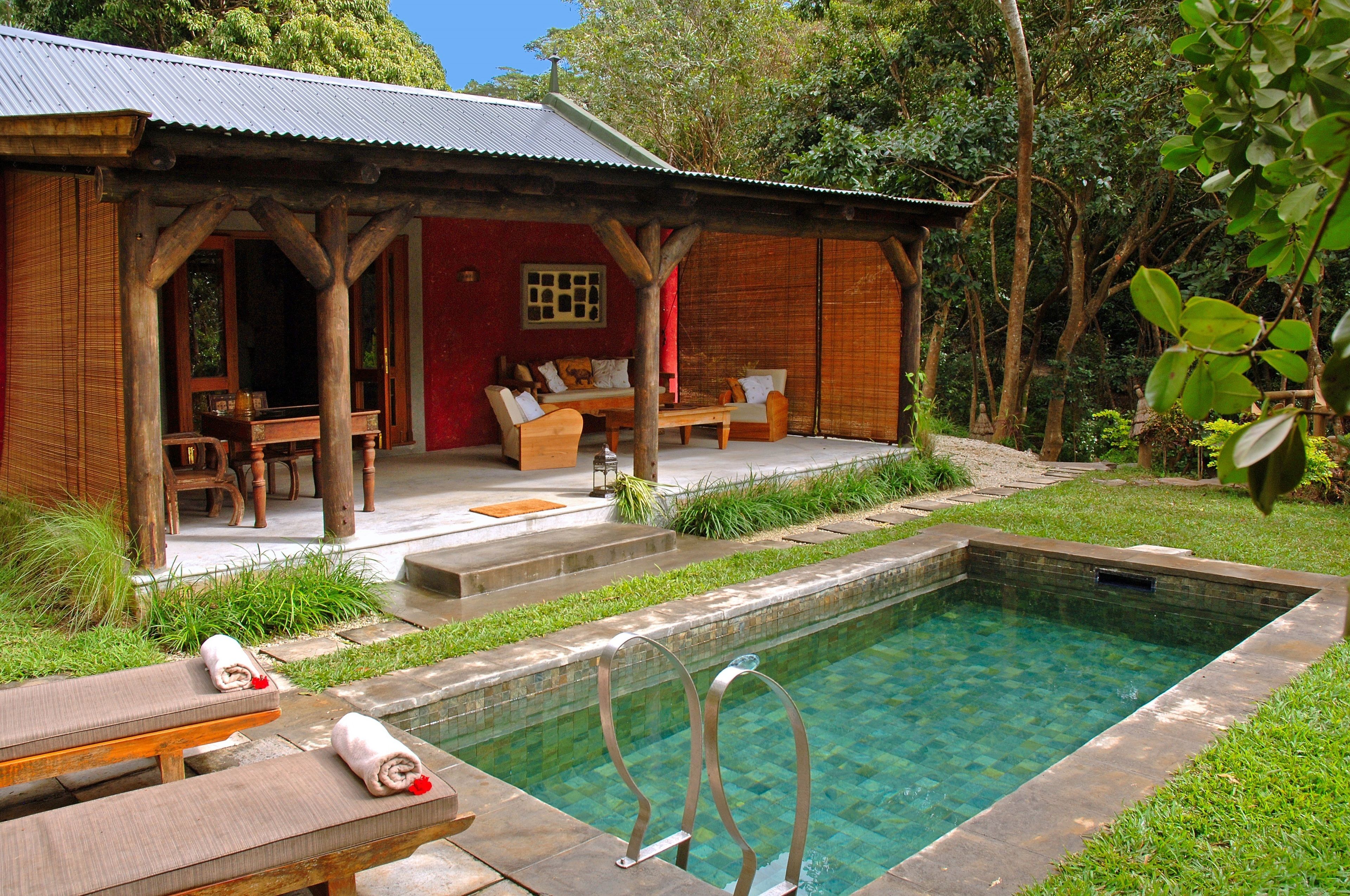 A wooden house with a pool, outdoor seating, and a red wall.
