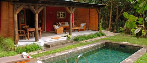 A wooden house with a pool, outdoor seating, and a red wall.