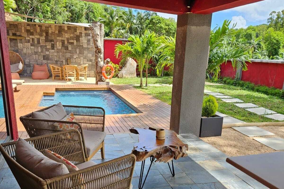 Área externa coberta com móveis de vime, piscina e um muro de pedra.