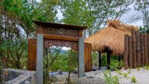 Una struttura in legno con tetto di paglia, immersa nel verde e circondata da elementi in pietra.