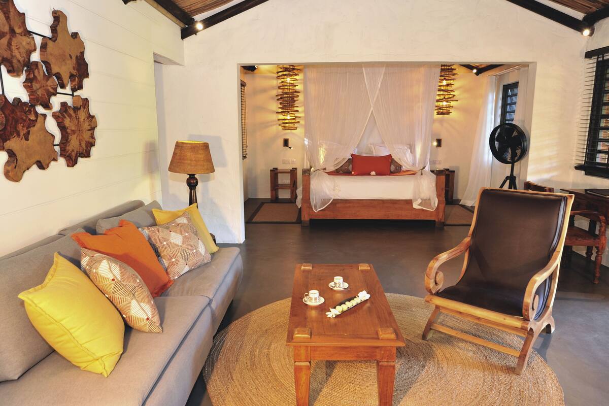 Quarto com sofá, cadeira de madeira, mesa de centro e cama com dossel.