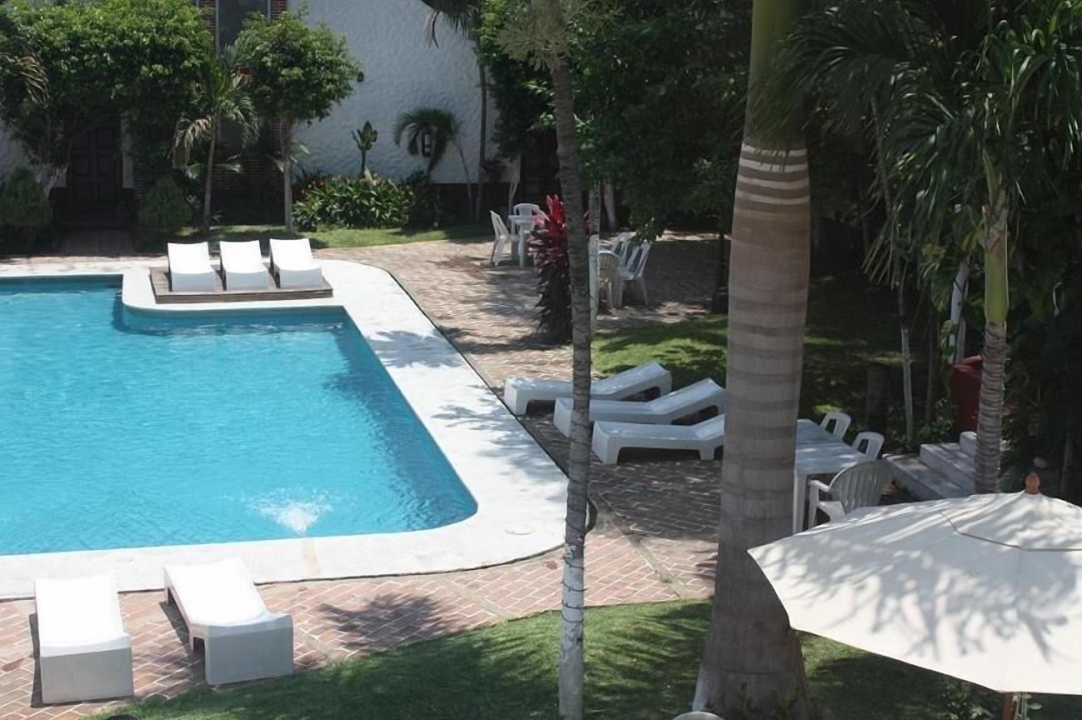 Una piscina rectangular con sillones de descanso blancos y una sombrilla.