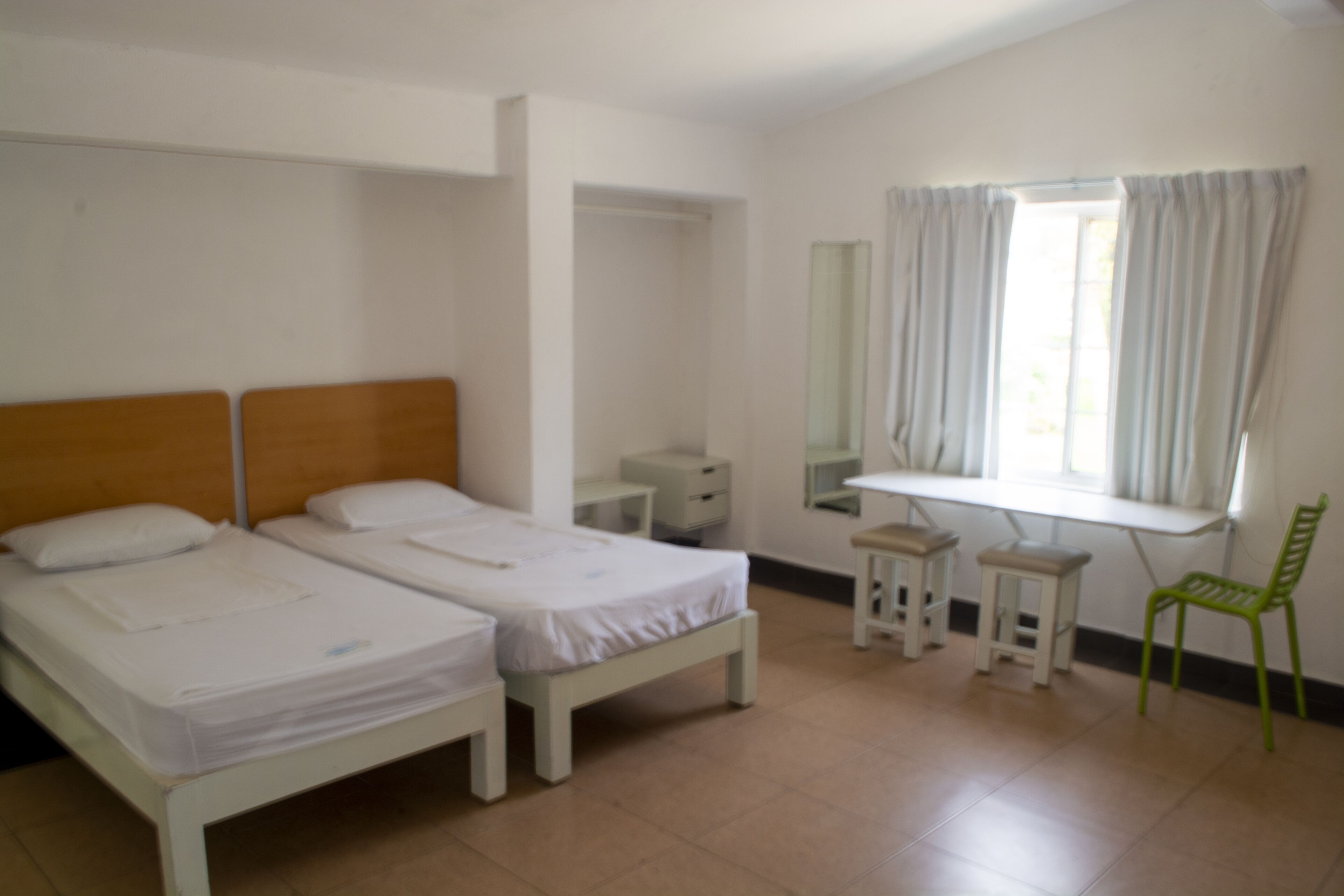 A room with two beds, a desk, a chair, a mirror, and a window with curtains.