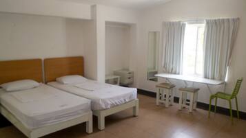 A room with two beds, a desk, a chair, a mirror, and a window with curtains.