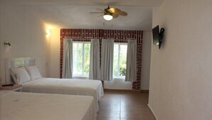 Habitación de hotel con dos camas, un ventilador de techo, un televisor y una ventana con cortinas.