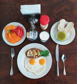 A breakfast setting with plates of eggs, beans, and toast, along with condiments and utensils. - HI Hotel Impala (Querétaro)