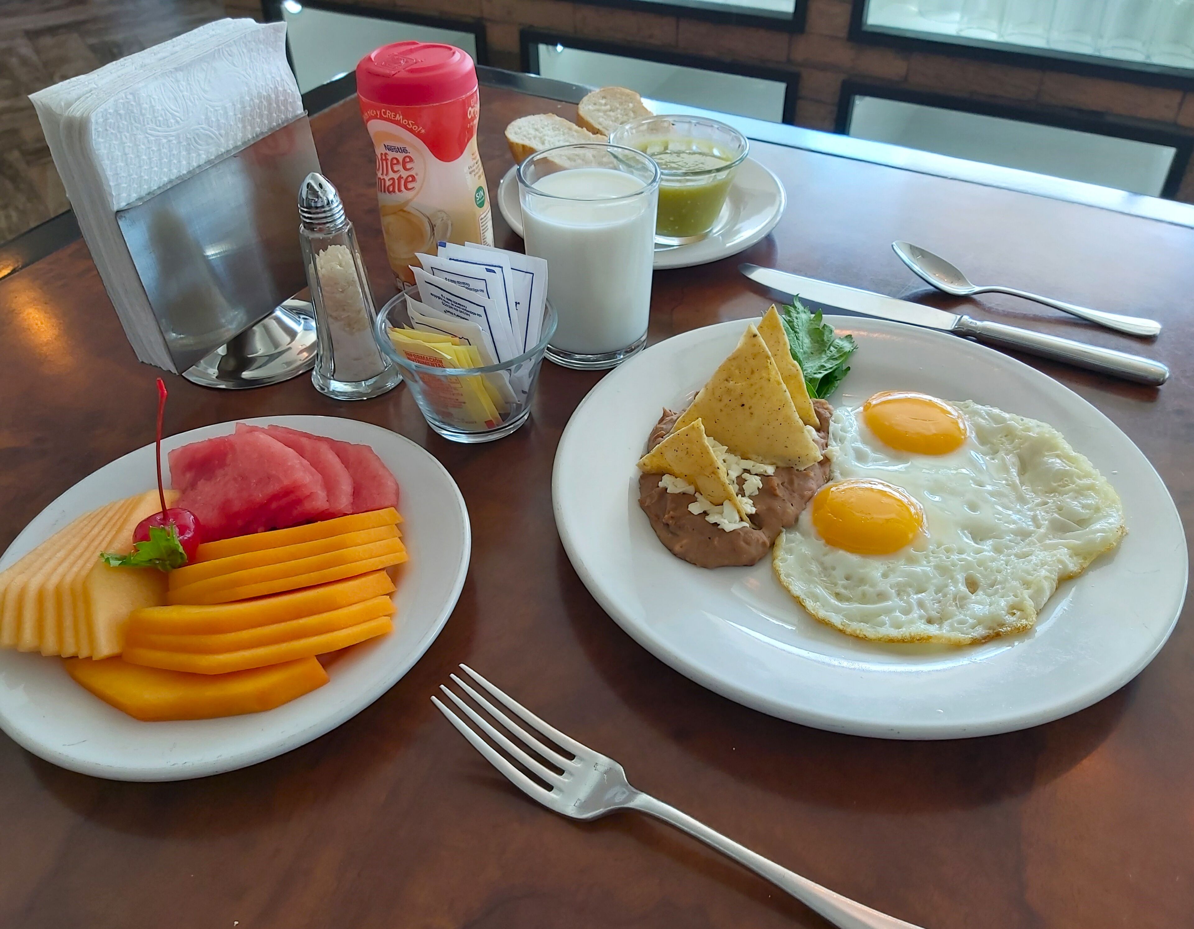A breakfast setting with plates of food, a coffee creamer bottle, a glass of milk, and condiments on a table.