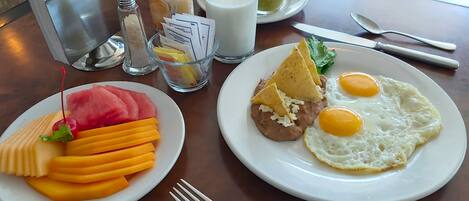 A breakfast setting with plates of food, a coffee creamer bottle, a glass of milk, and condiments on a table.