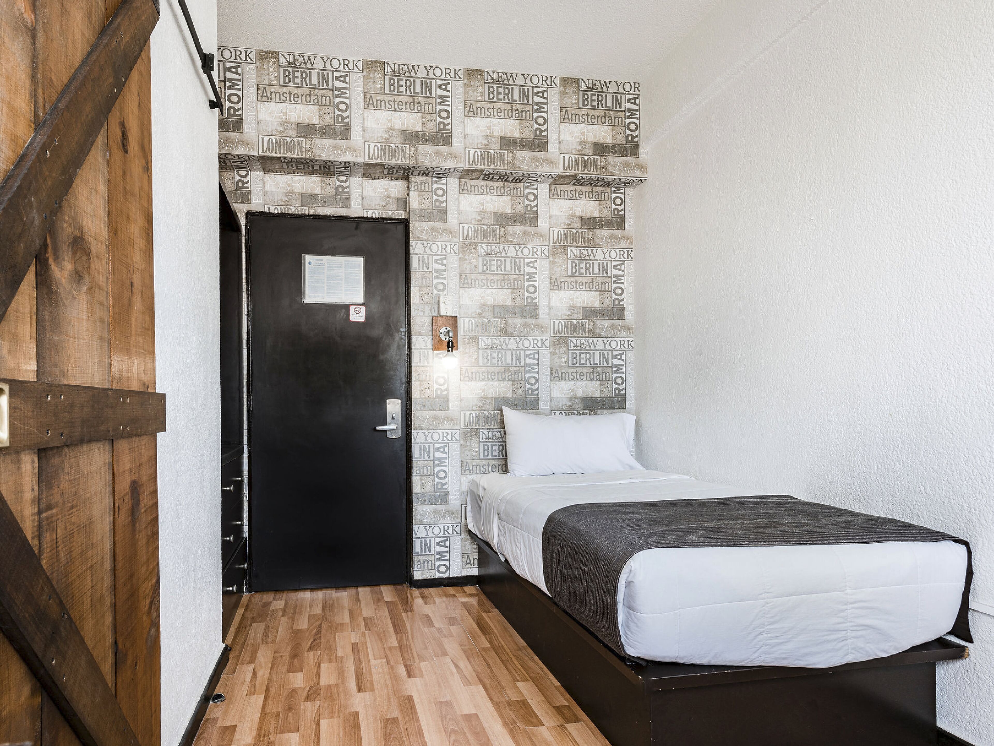 Un dormitorio con cama, una puerta de madera y un papel tapiz con nombres de ciudades.