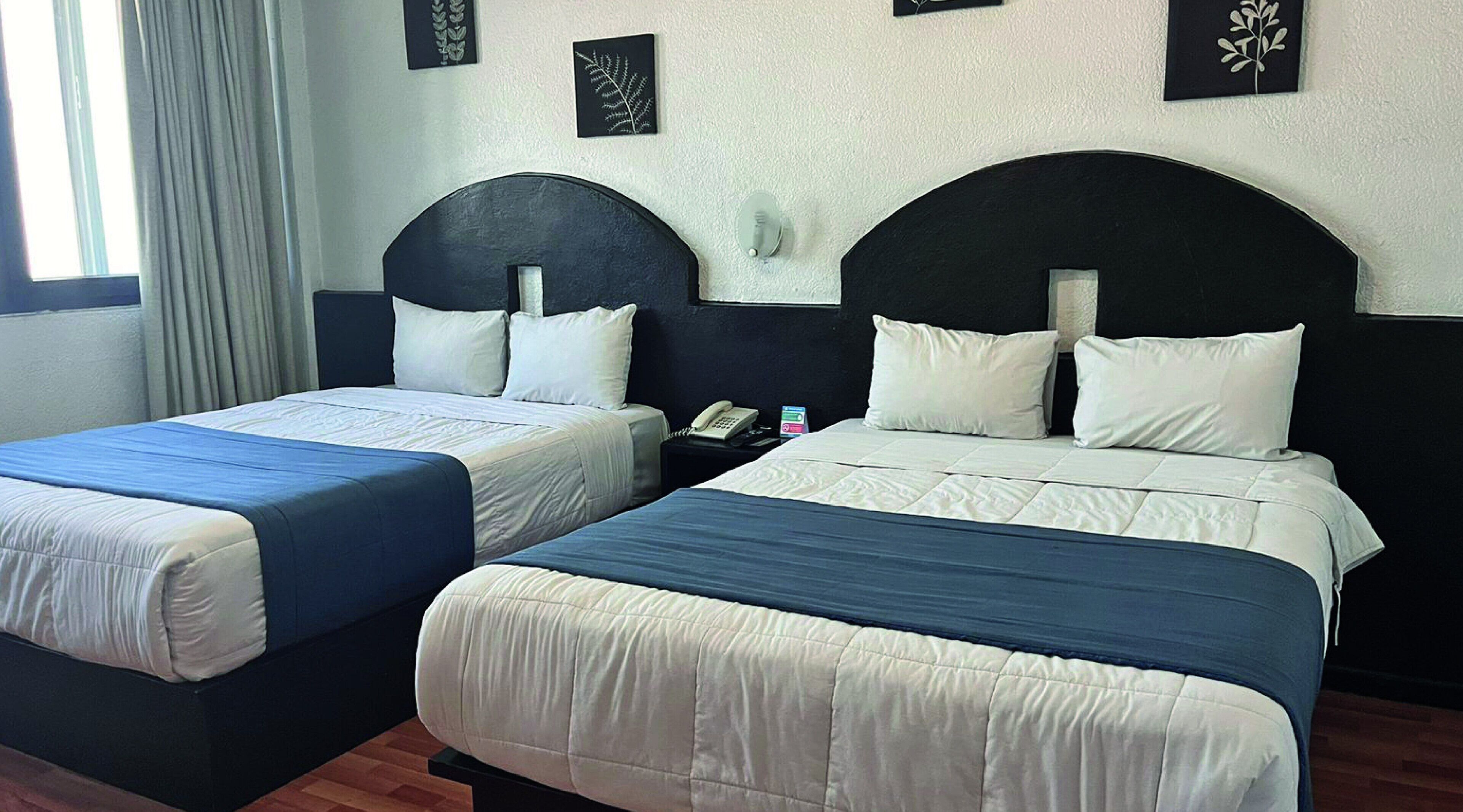 Two single beds with headboards, a bedside table with a phone and a card, and a window with curtains.
