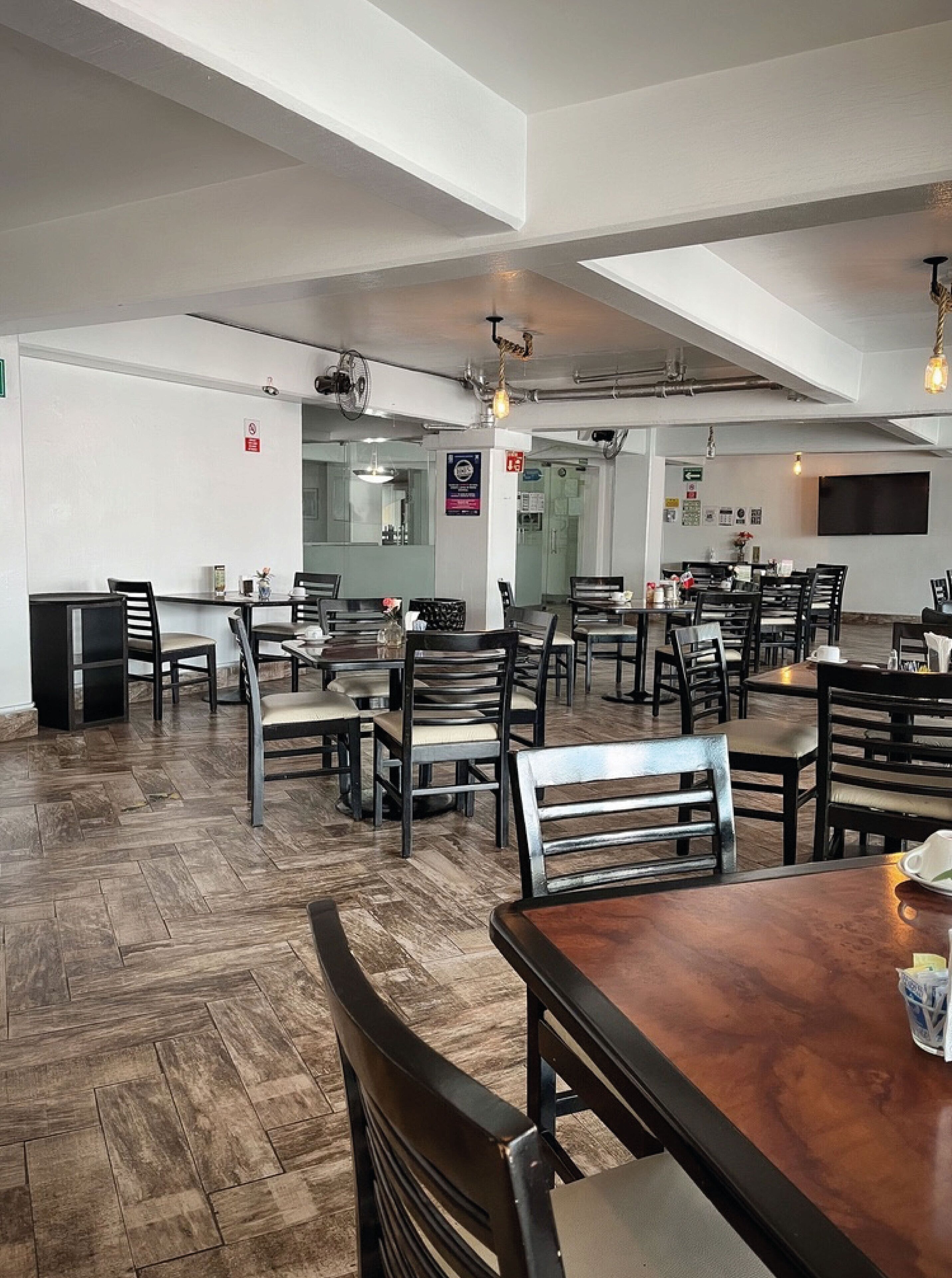 Un restaurant spacieux avec de hauts plafonds et des conduits apparents. Les tables et les chaises sont disposées pour accueillir les clients.