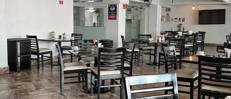 A spacious restaurant with high ceilings and exposed ductwork. Tables and chairs are arranged for dining.