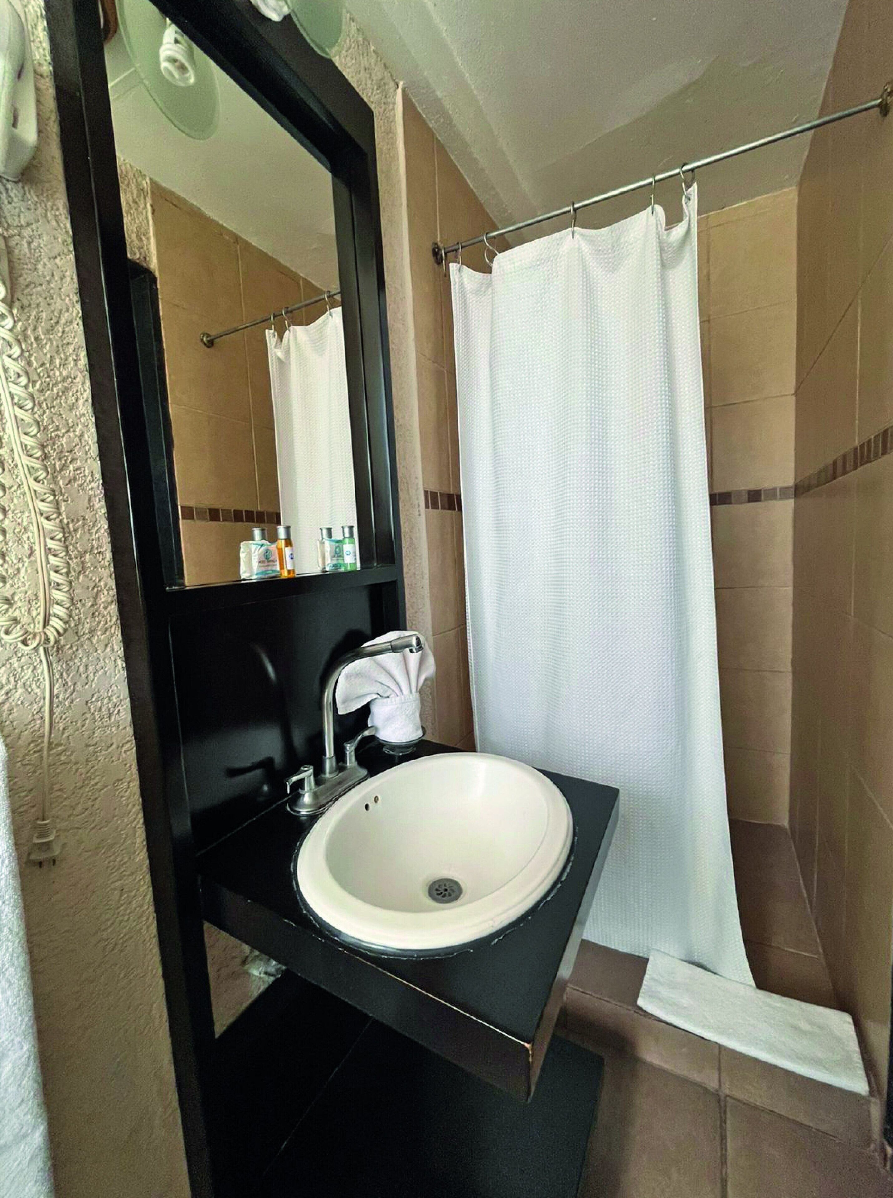 A bathroom with a white sink, a black countertop, a mirror, and a shower curtain.