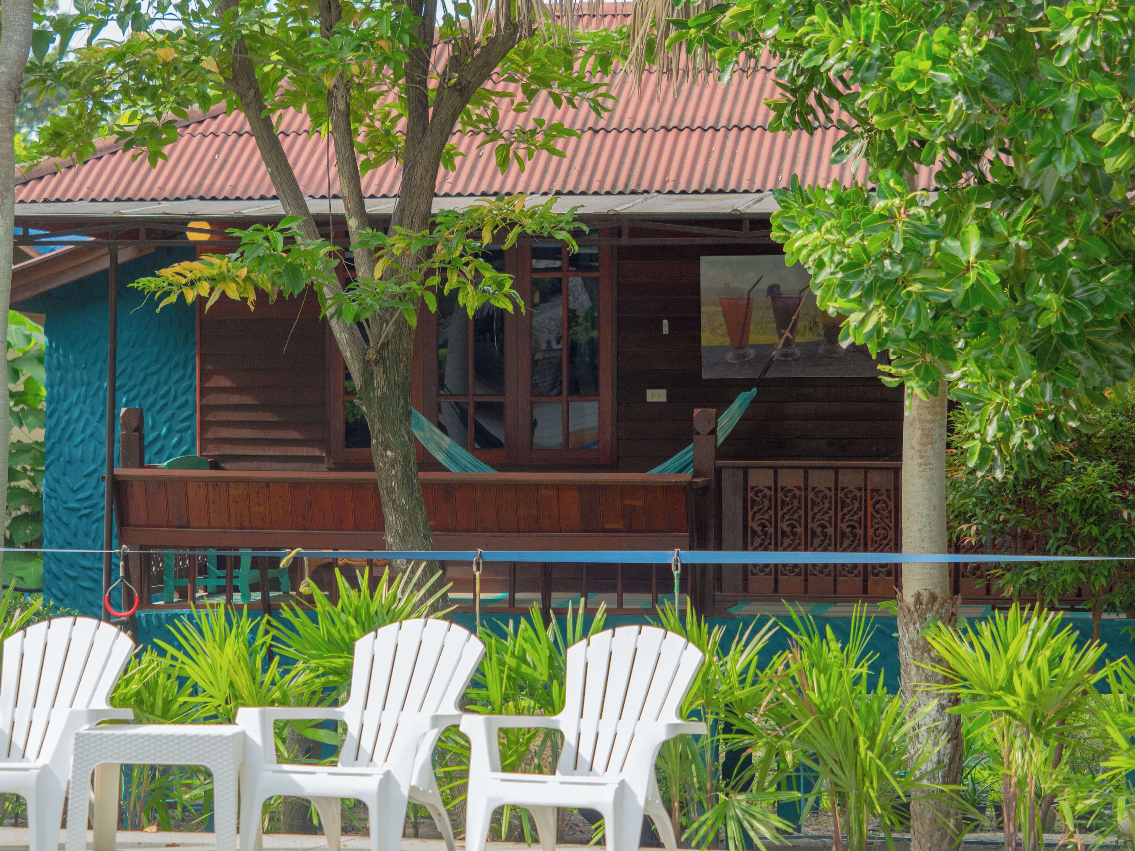 A wooden building with a red roof, a balcony, and white plastic chairs in front.