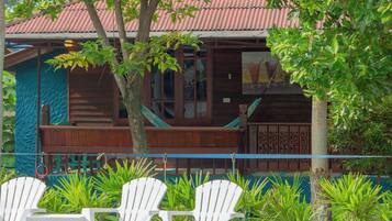 A wooden building with a red roof, a balcony, and white plastic chairs in front.