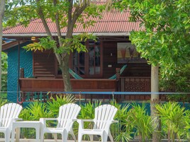 A wooden building with a red roof, a balcony, and white plastic chairs in front.