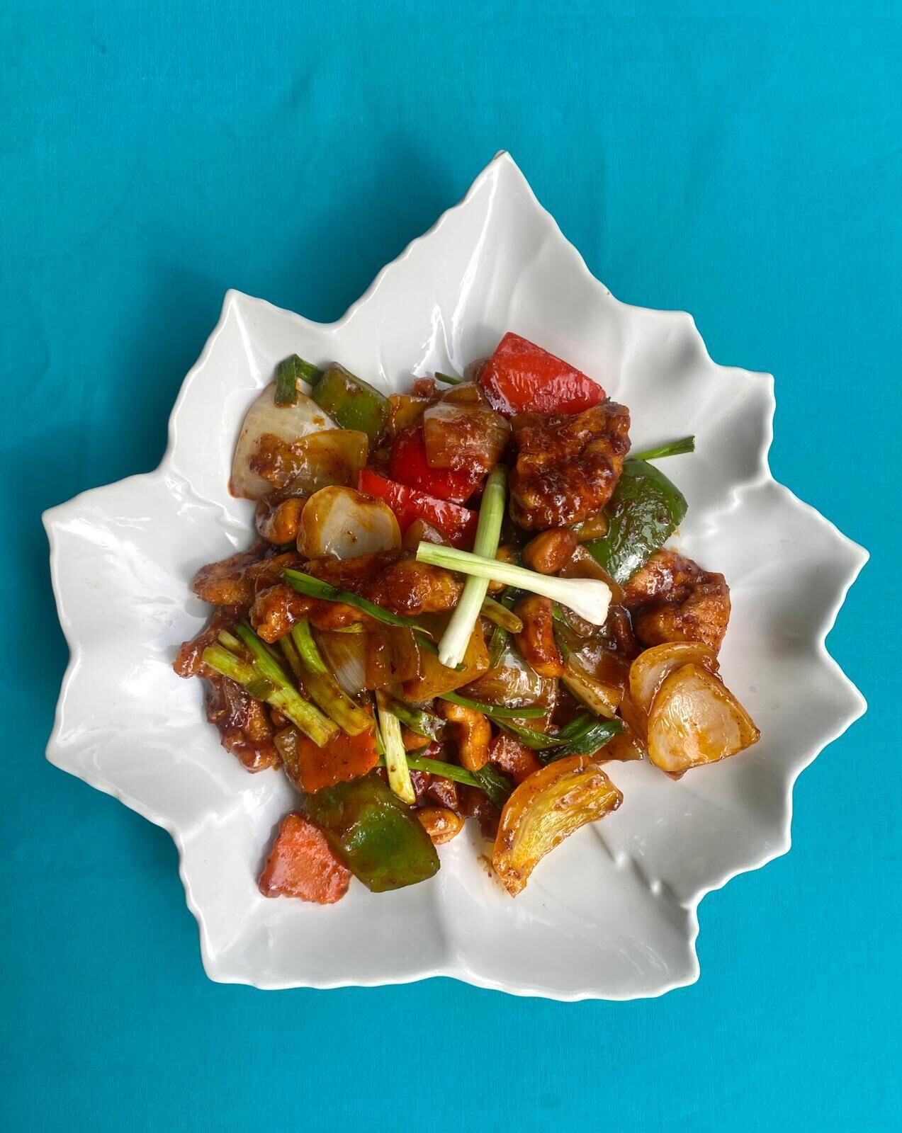 A dish of stir-fried vegetables and meat on a white plate with a blue background.