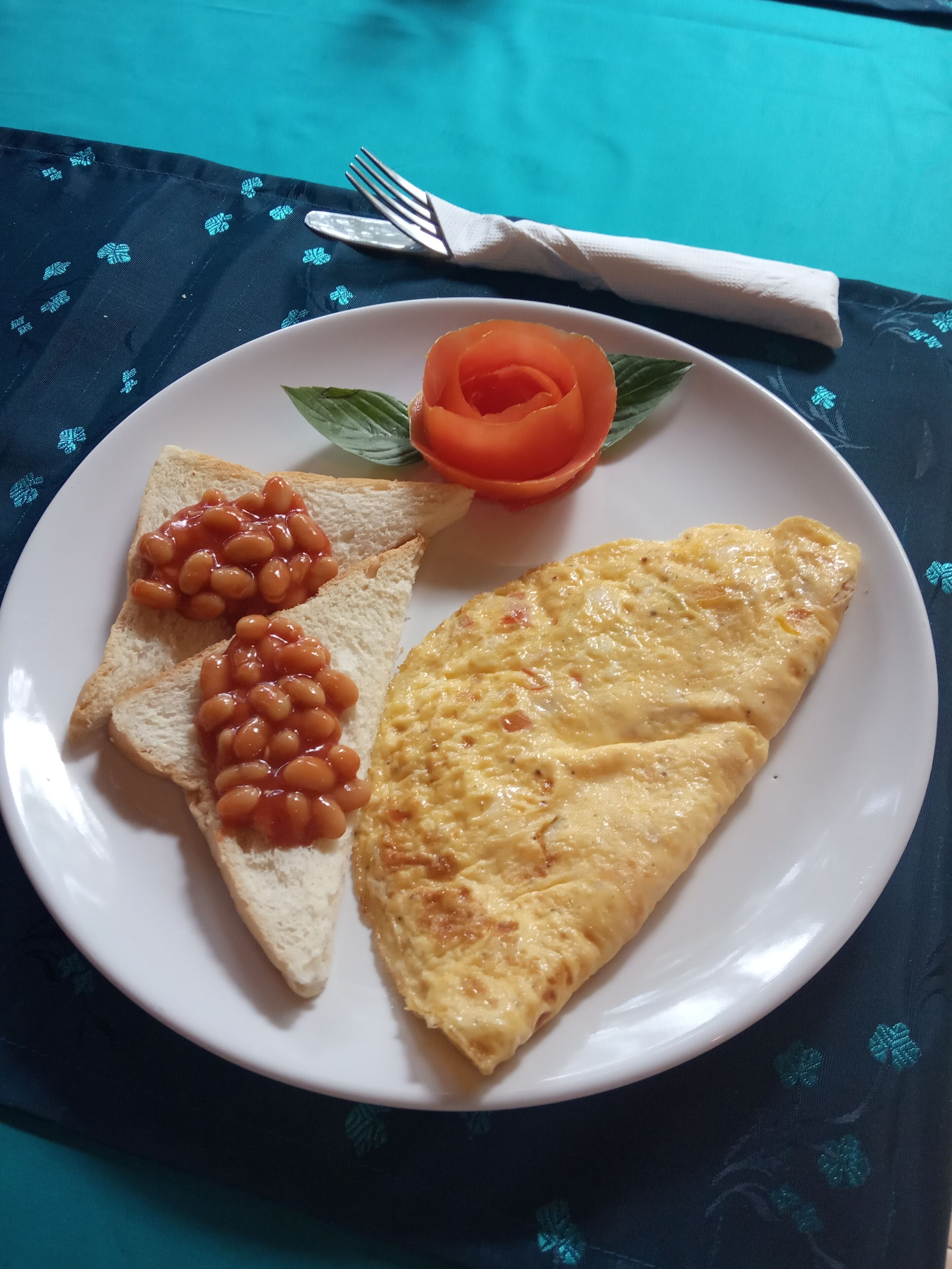 Um prato com torradas, feijão e uma omelete, acompanhado de um garfo e uma faca sobre uma toalha de mesa.