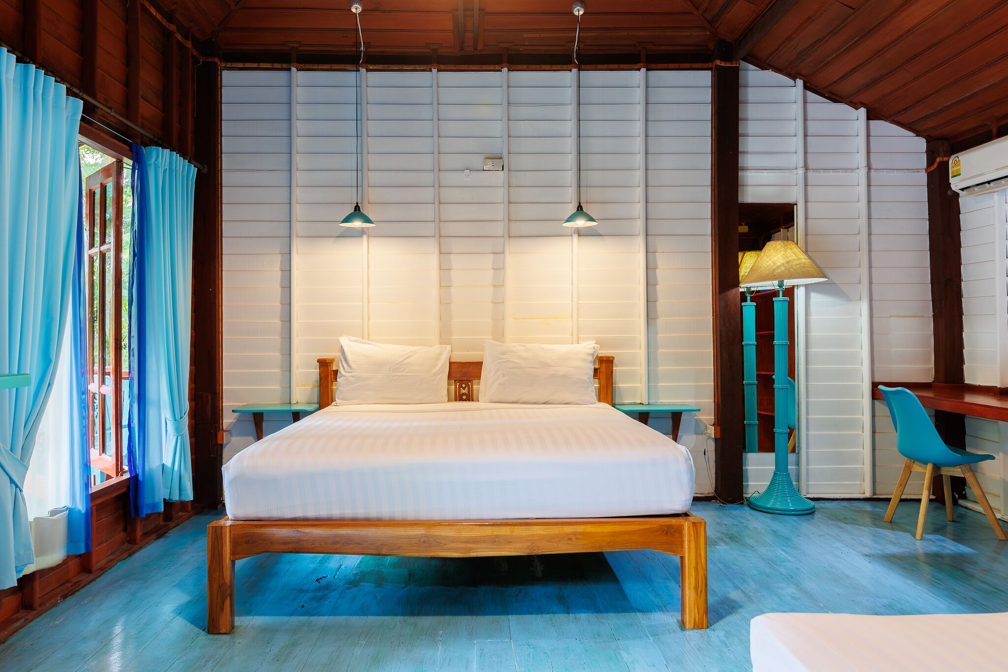 A bedroom with a wooden bed, two bedside lamps, a blue chair, and a floor lamp.