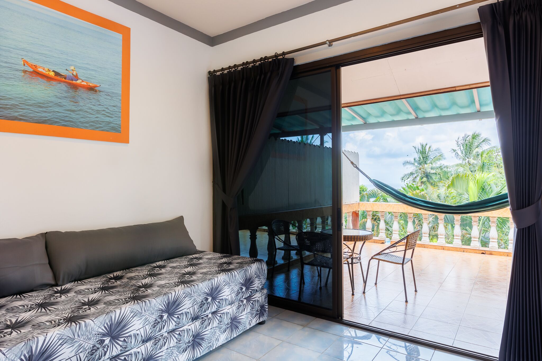 A room with a bed, a sliding glass door leading to a balcony with a hammock and chairs.