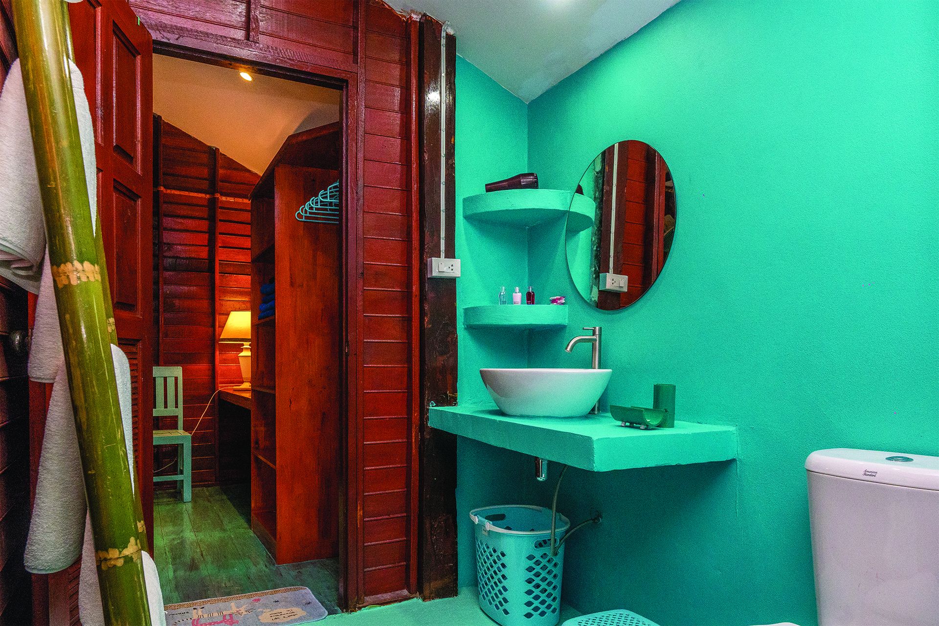 A bathroom with a green wall, a white sink, a mirror, and a toilet.