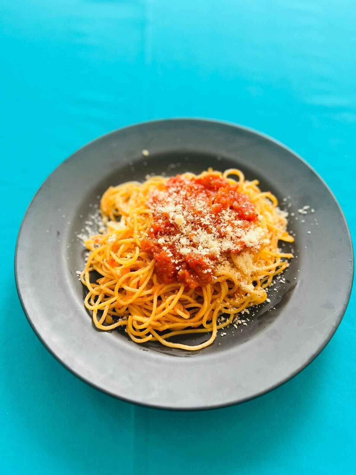 A plate of spaghetti with tomato sauce and grated cheese on a dark plate.