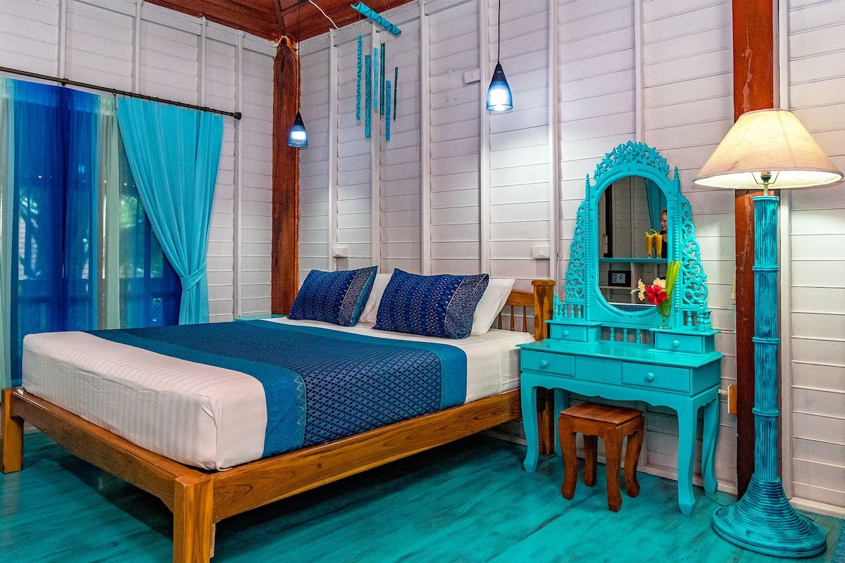 Une chambre à coucher avec un lit en bois, une commode turquoise et un miroir avec une lampe.