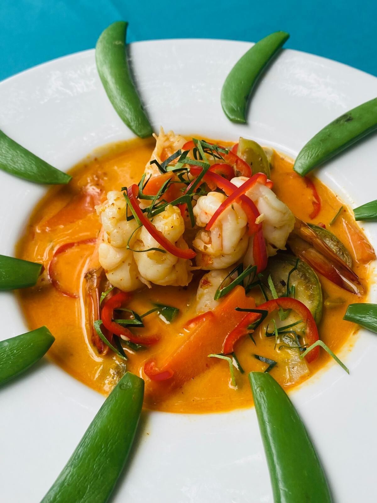 Un plato de camarones y vegetales en salsa cremosa, adornado con pimientos rojos y hierbas verdes.