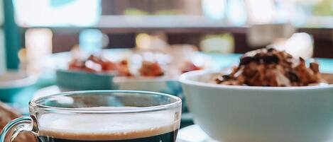 Une tasse de café en verre, posée sur une soucoupe avec une cuillère, sur une table recouverte d’une nappe de couleur turquoise.