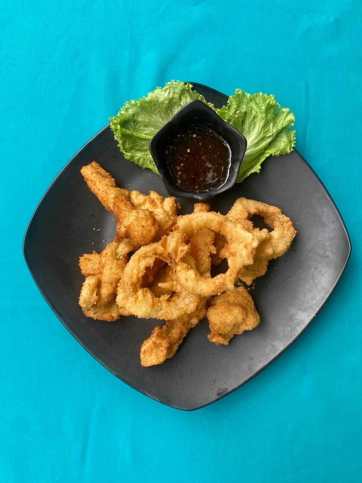 Un plato de calamares fritos, acompañado de salsa y hojas de lechuga.