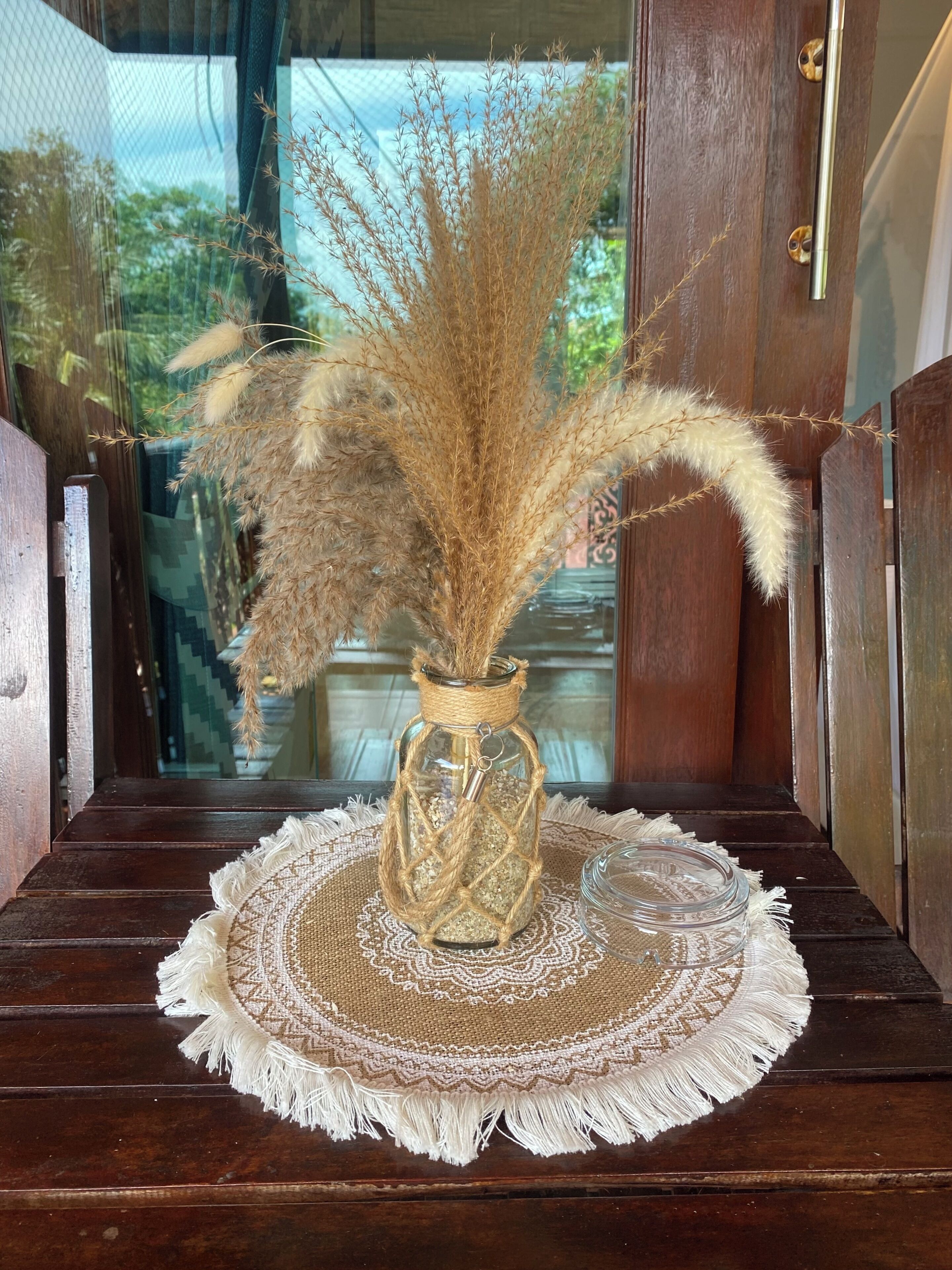 A rustic wooden bench with a decorative glass vase containing dried pampas grass.