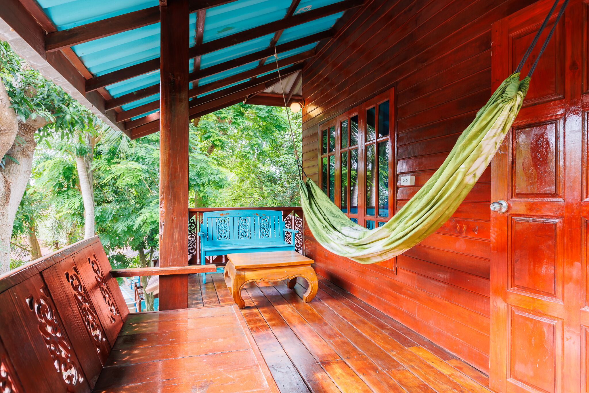 A wooden deck with a hammock, a bench, and a view of lush greenery.