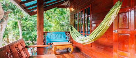A wooden deck with a hammock, a bench, and a view of lush greenery.