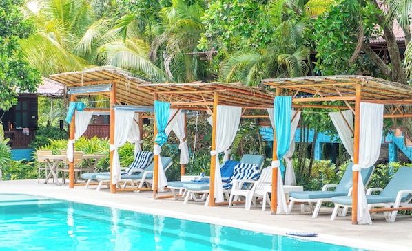 Un área junto a la piscina con sillones de descanso y toldos.