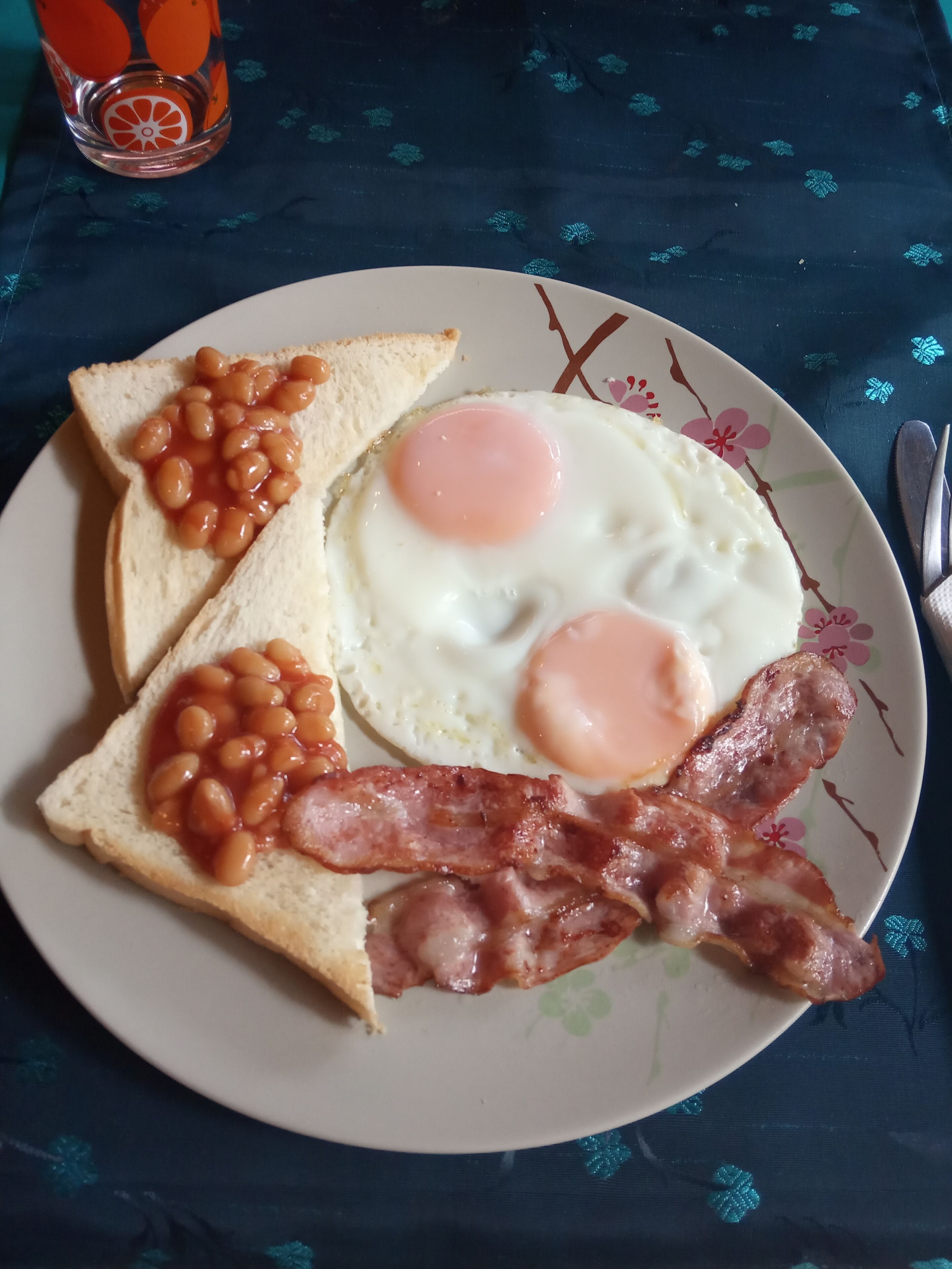 Un plato con tostadas, frijoles, dos huevos fritos y tocino.