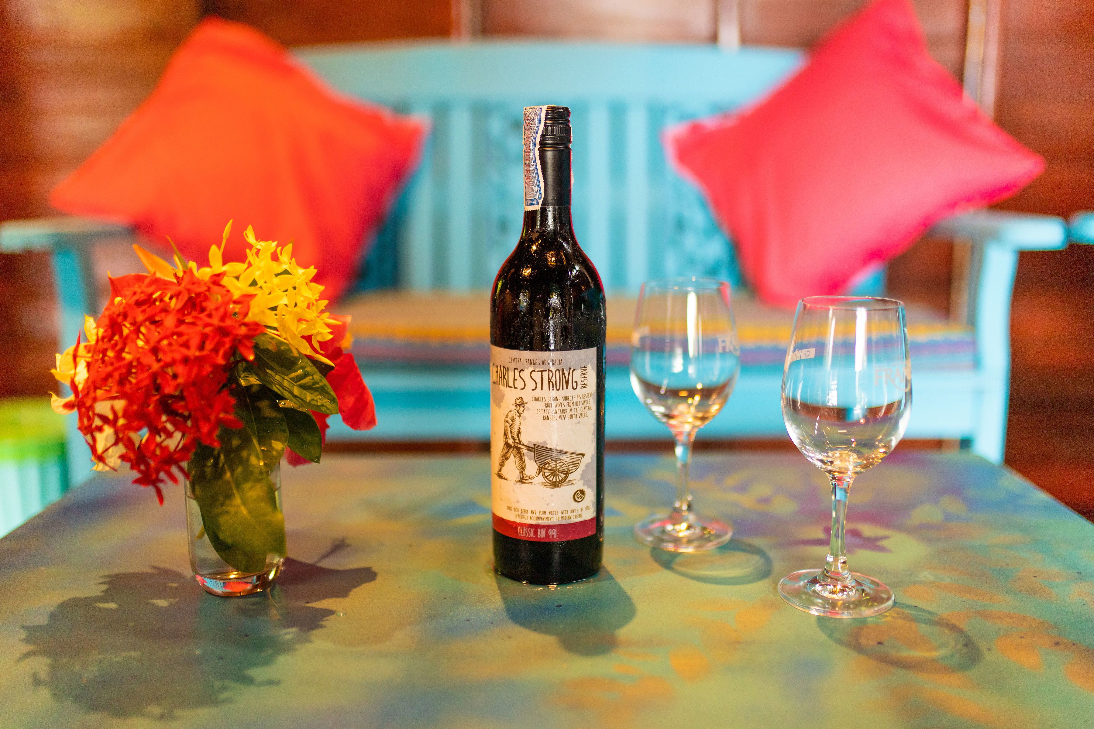 A bottle of Charles Strong wine, a glass of wine, and a vase with flowers on a table.