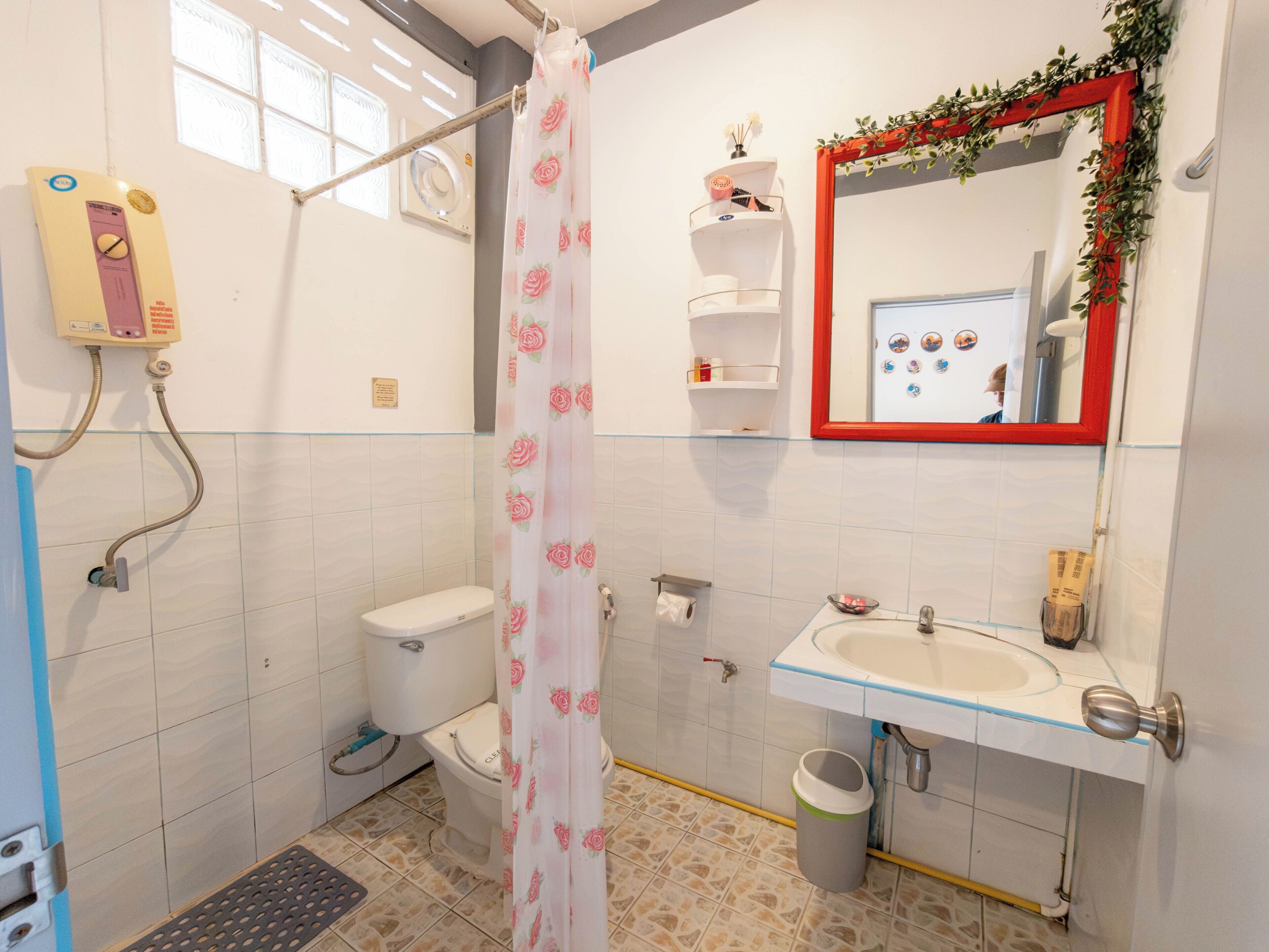 A bathroom with a toilet, shower, sink, and a mirror with a red frame.