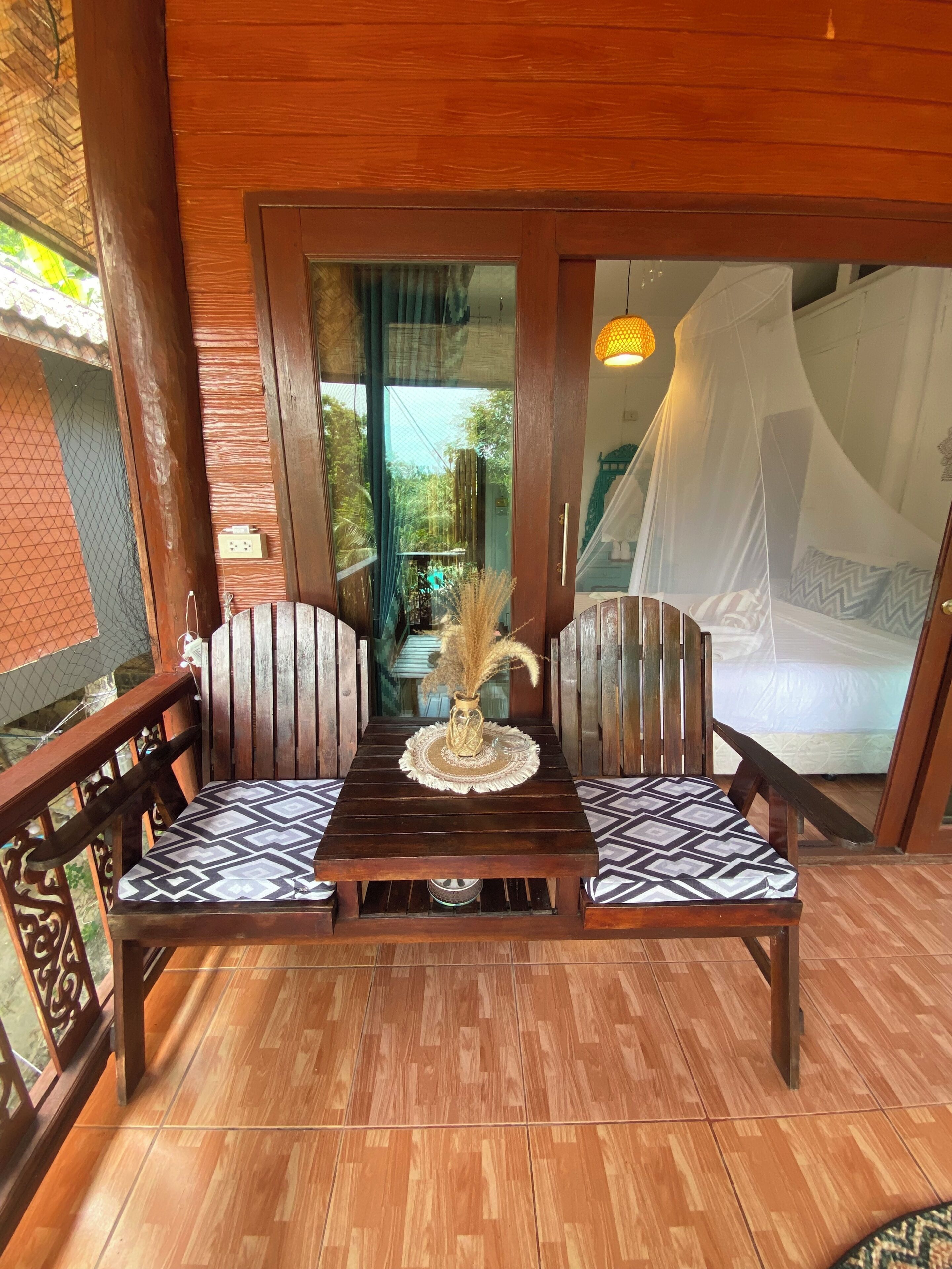 A wooden balcony with a table and chairs, a view of the garden, and a bed with a canopy.