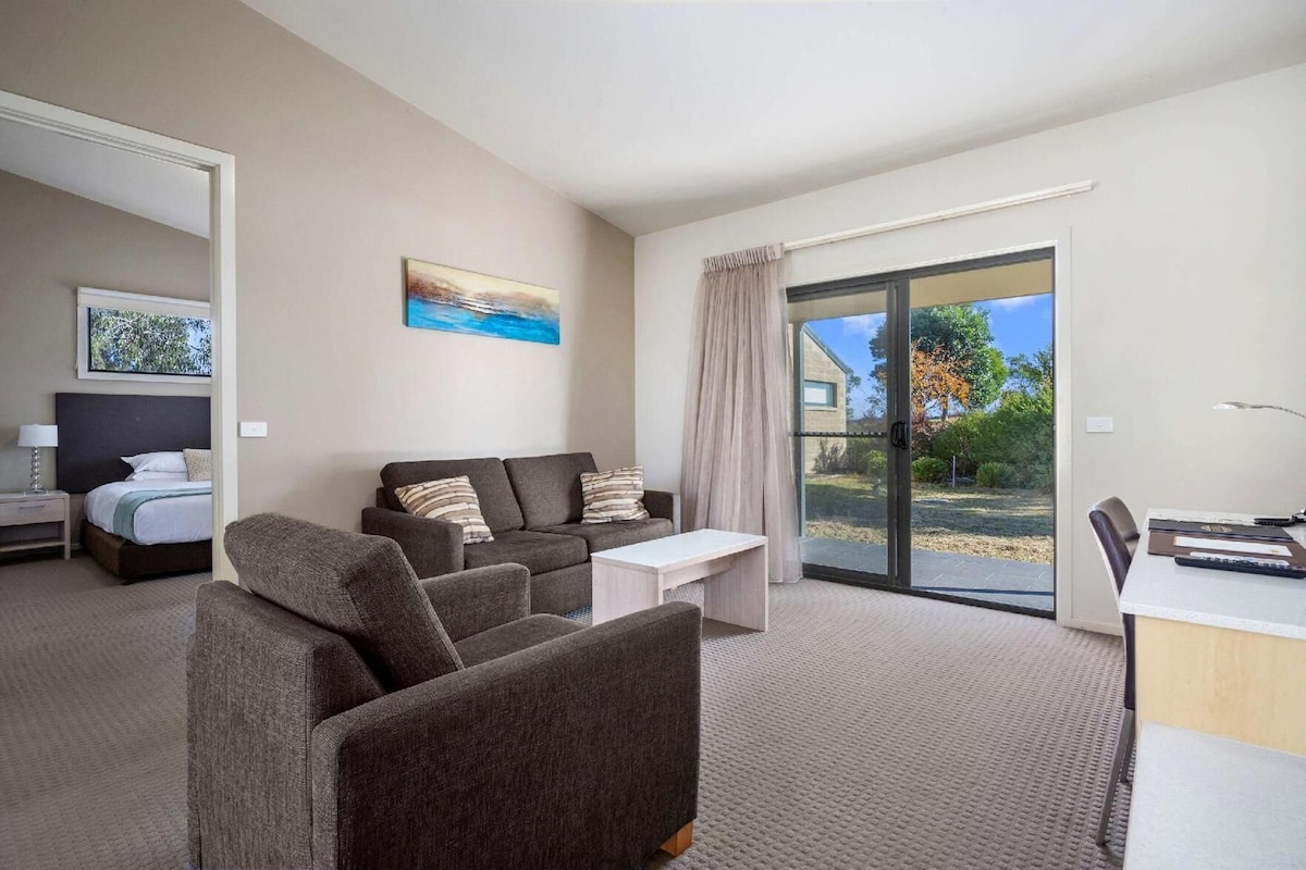 A modern hotel room with a sofa, a bed, a desk, and a view of the outdoors.