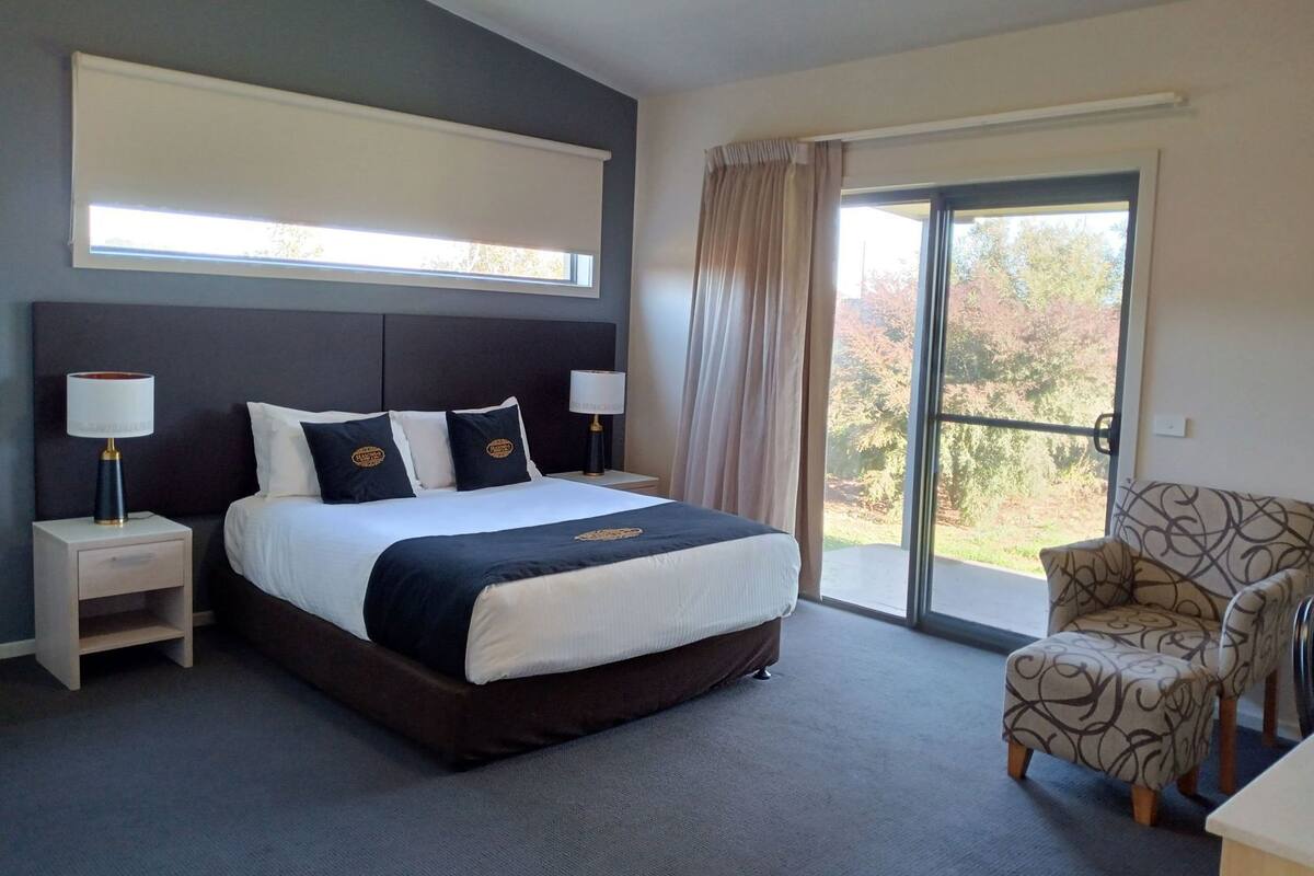A hotel room with a large bed, two bedside tables with lamps, a chair, and a sliding glass door to the outside.