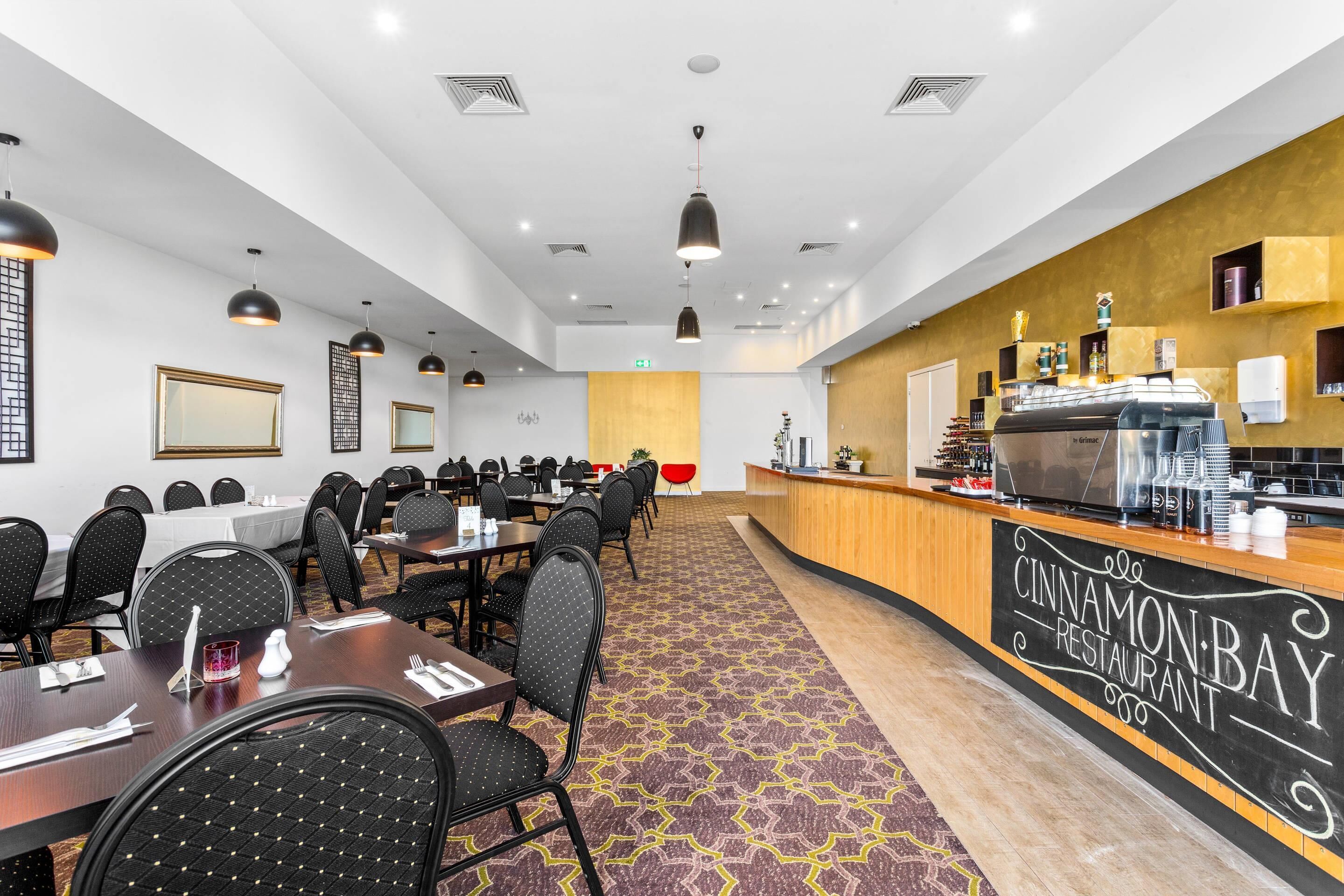 Un comedor de hotel con mesas, sillas, una recepción y una máquina de café.